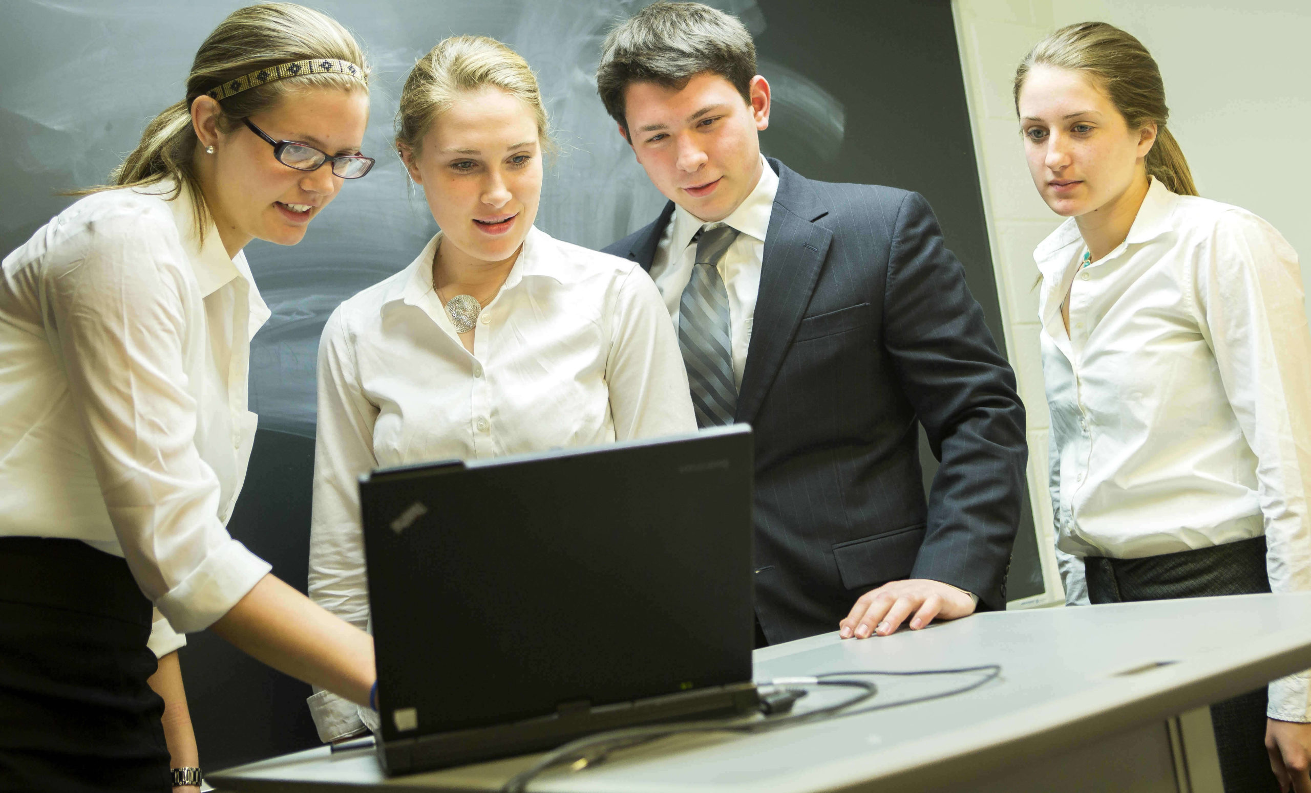 Professionally-dressed students gathered around a laptop