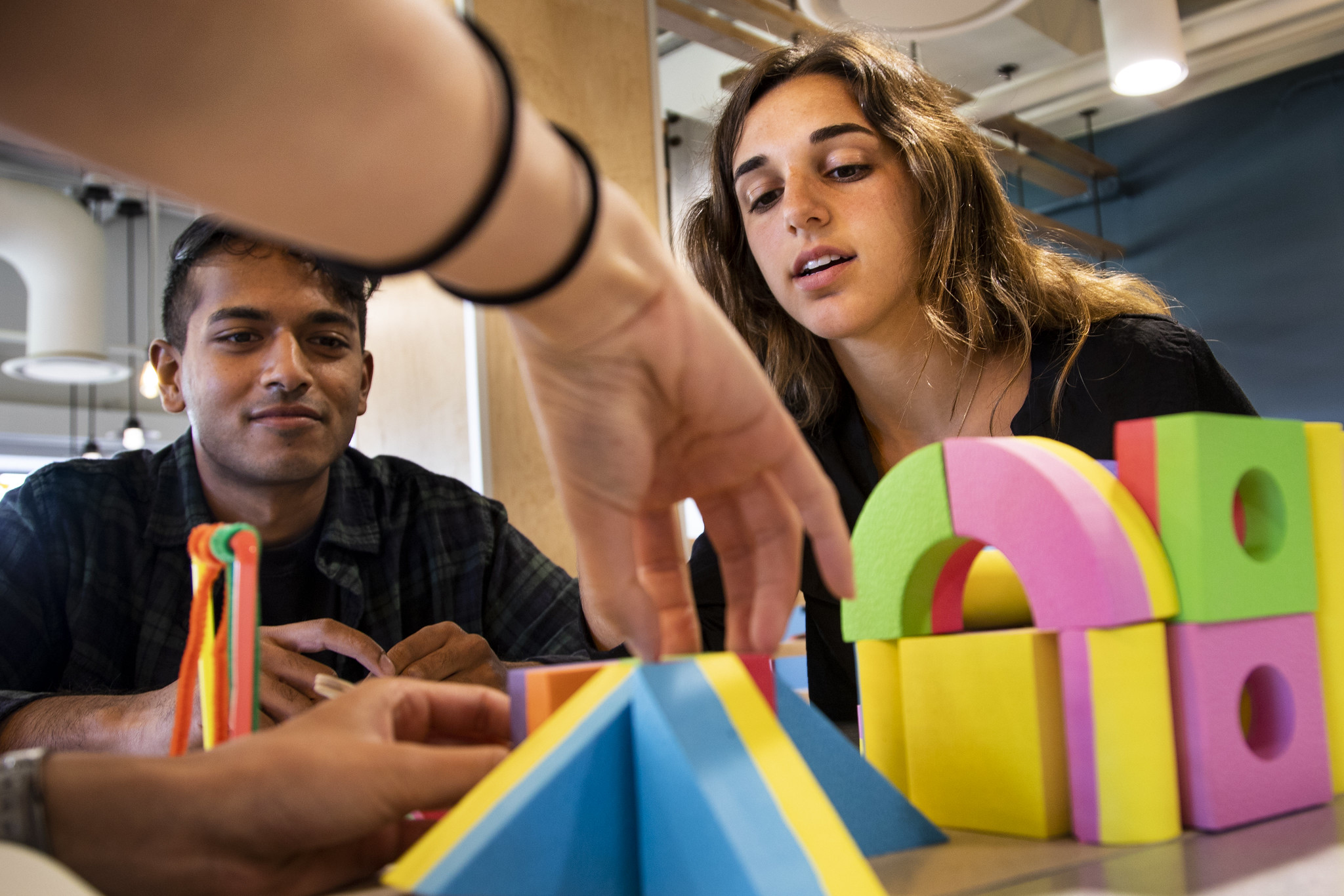 Front view of hand placing a colorful block while other students observe