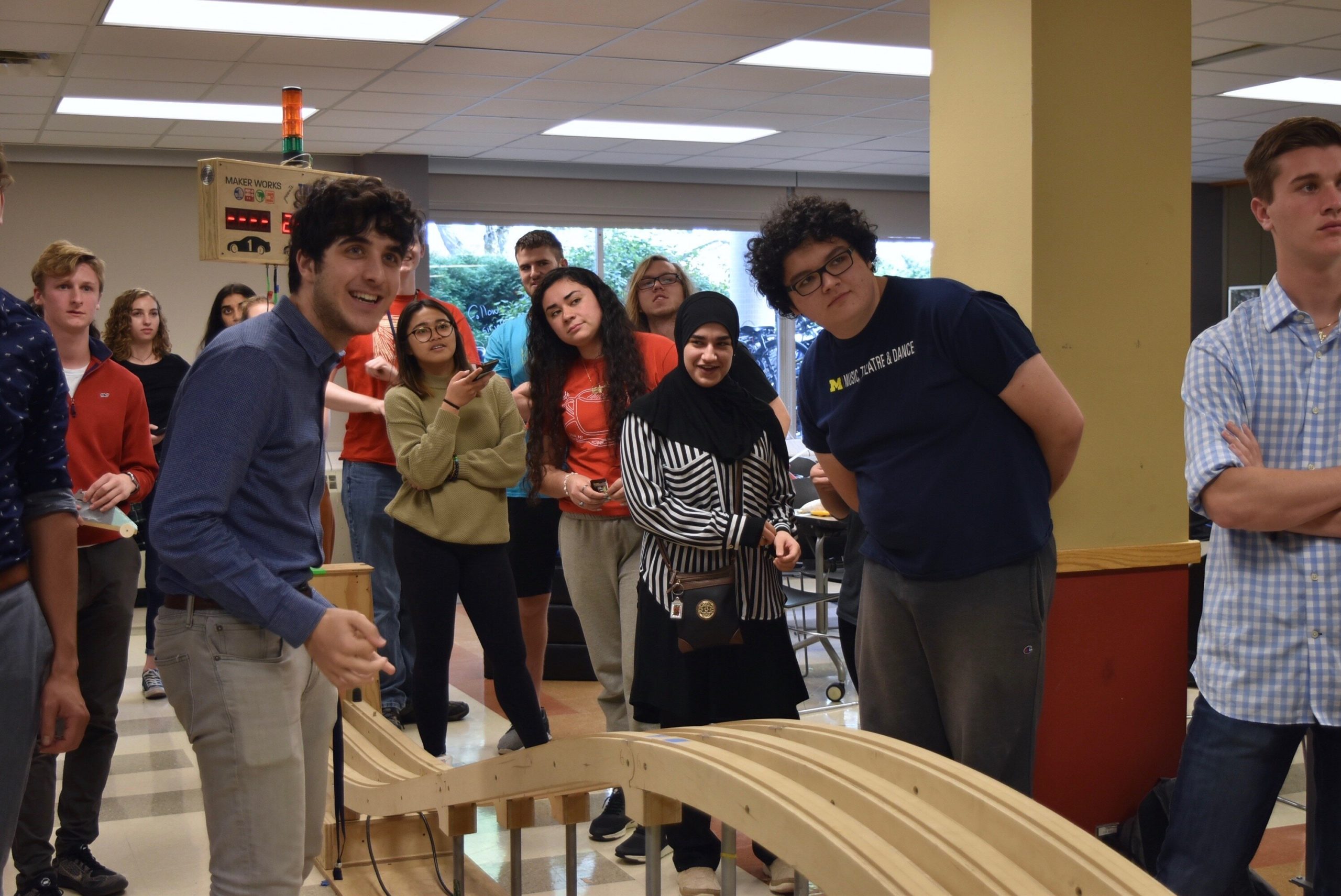 A group of students gathered around a wooden race track, anticipating the results