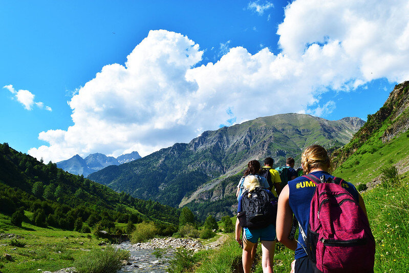 Back view of students in a line hiking along a mountain with a blue sky and clouds