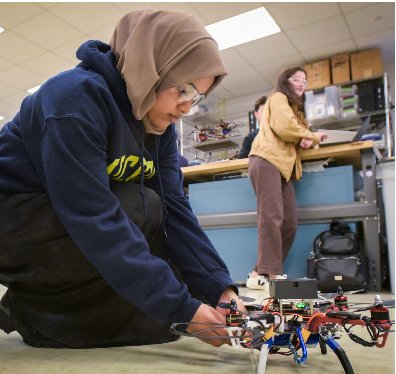 Student wearing hijab kneeling on ground working on drone