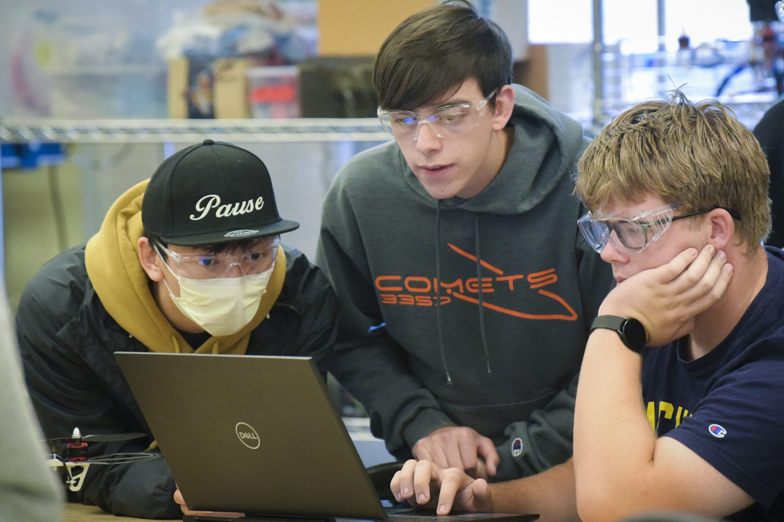 Three students wearing goggles looking at one laptop screen