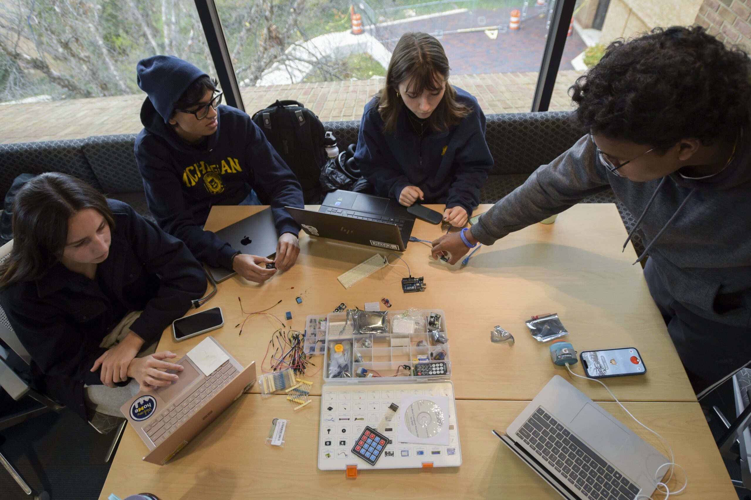 Aerial view of four students working on laptops with parts scattered on table