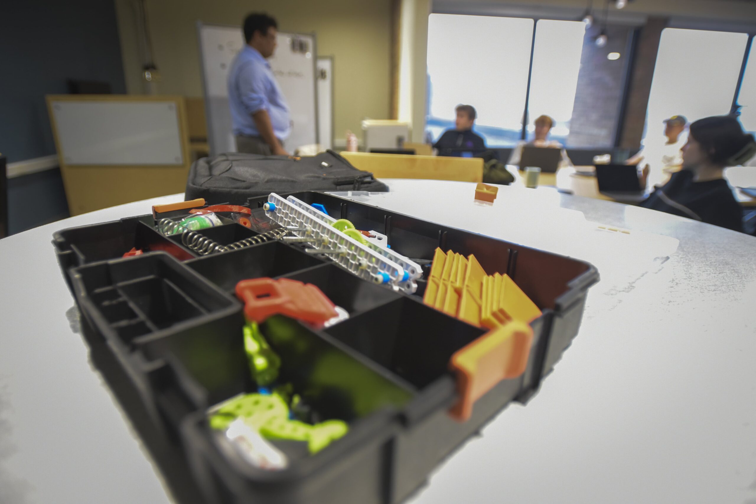 Black toolbox filled with colorful parts on table in front of classroom