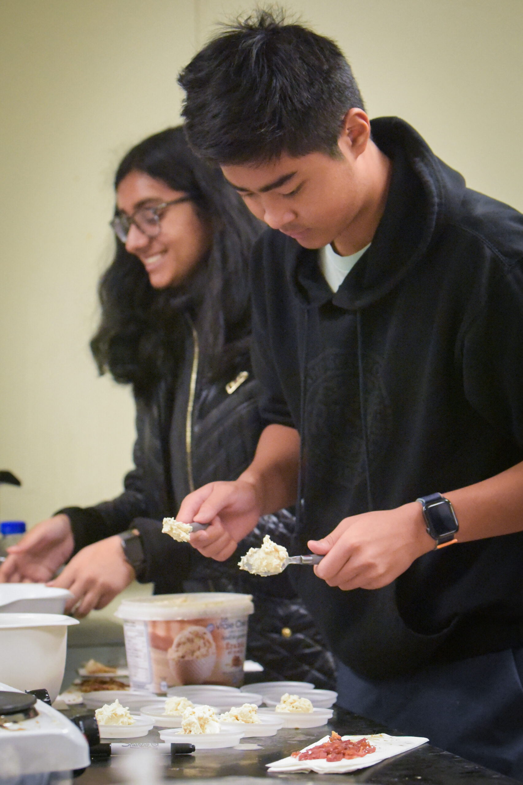 Two students scooping mashed food product onto small plastic dishes