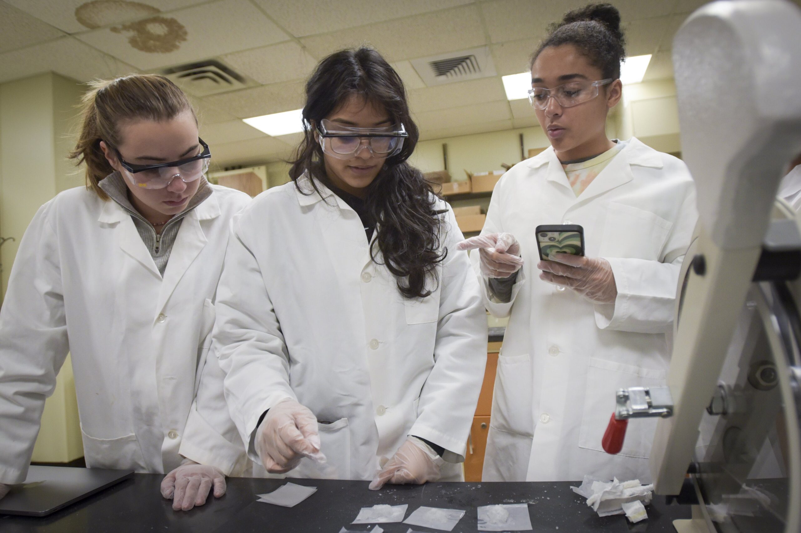 Three students in lab attire discussing results of lab experiment