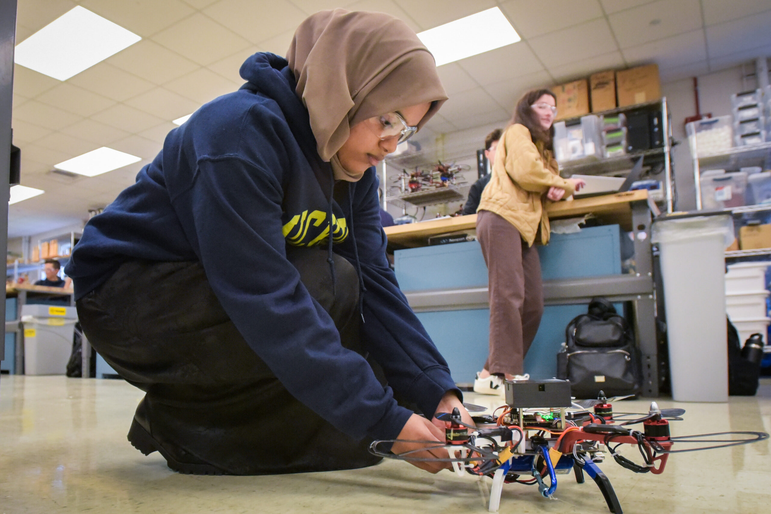 Student wearing hijab kneeling on ground working on drone