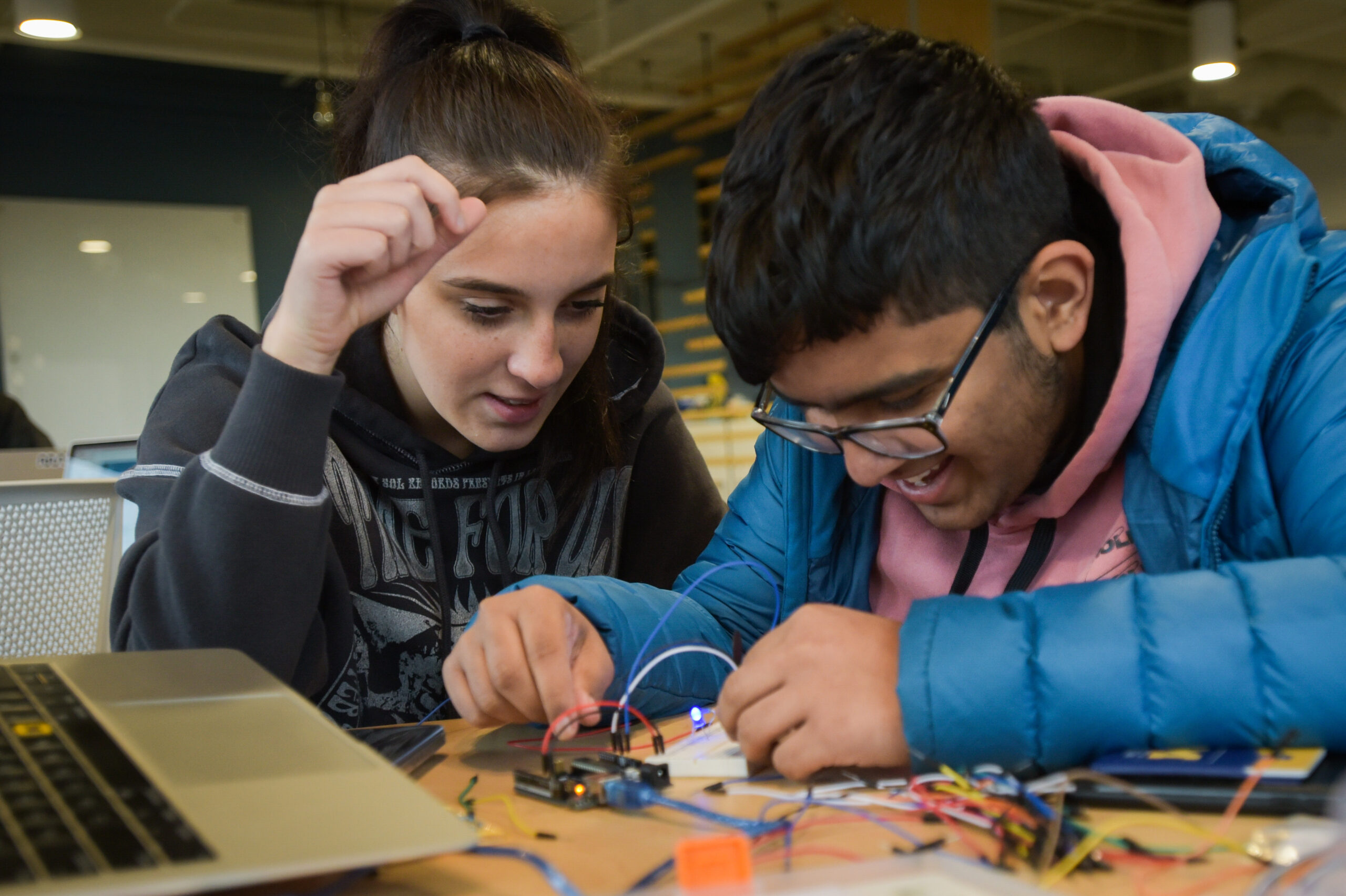 Two students huddled over connecting wires, turning on a small LED