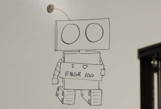 Drawing of a robot holding sign that says “I love ENGR 100” on whiteboard
